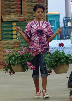 Girl in pink-purple tie dye carrying two hanging baskets of flowers